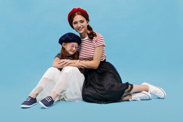 Beautiful lady in good mood with cute smile in black stylish skirt and white sneakers sitting on floor and posing with little girl..