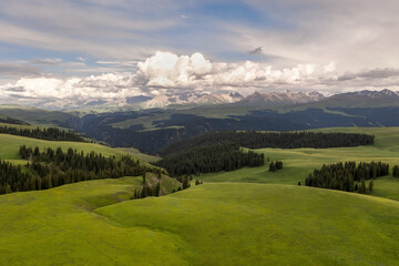 Mountain peaks and grassland are under white clouds.