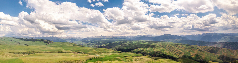 Fototapeta premium Mountain peaks and grassland are under white clouds.