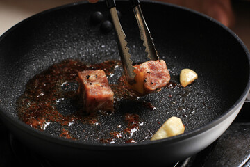 Cooking Process, Grilled Wagyu Fatty Saikoro Cubed Dice Beef Steak with Barbeque Sauce on Black Pan using Stainless Tongs. Steak Spice with Black Pepper and Salt