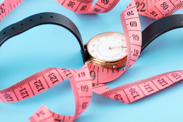Tape measure and watch on blue background