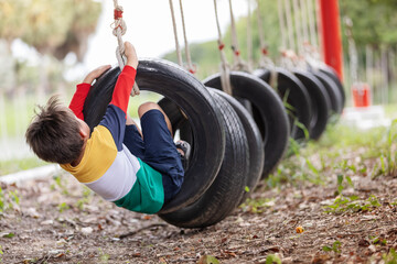 A boy wearing bright colored clothes playing tire swing hanging at playground and having fun...