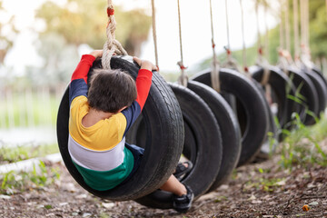 A boy wearing bright colored clothes playing tire swing hanging at playground and having fun...