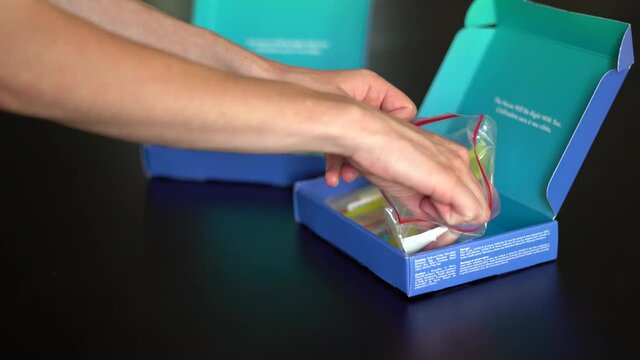 4K clip of woman's hands unpacking contents of a COVID19 home test kit on dark background. Second kit can be seen in background. Pandemic, testing, coronavirus, at home test kit.