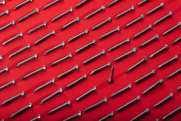 Obraz premium Black steel nails and nut on red background, arranged horizontally, concept of gender equality, be unique and stand out, inclusion 