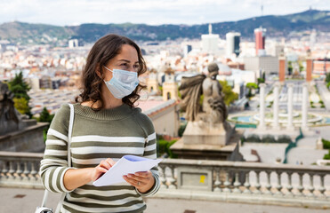 Young woman tourist in medical mask holding paper map in the city center of Barcelona