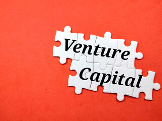 Finance concept.Text Venture Capital with jigsaw puzzle on a red background