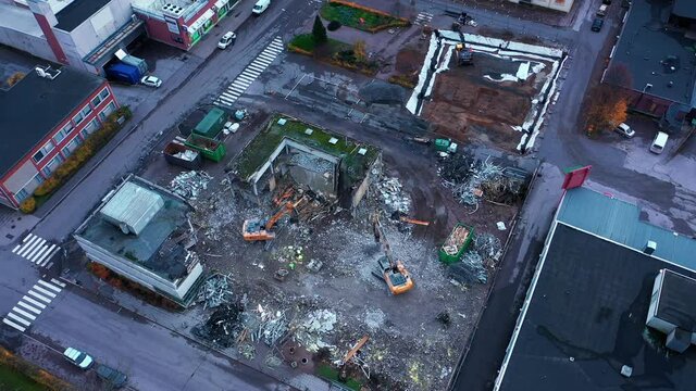 Aerial view around diggers dismantling a urban structure, dark day - orbit, drone shot