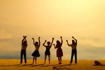 Fototapeta premium Miniature tiny people toys photography. Silhouette group of teens raised hand or hands up celebration on sunset time at the beach.