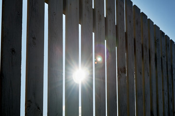 Close-up of a wooden fence on a sunny summer day. The sun shines through the fence