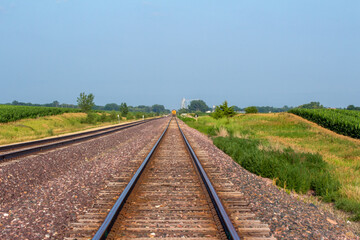 Fototapeta premium Landscape view of a double railroad track in a rural agricultural landscape on a sunny day, with fields in the background