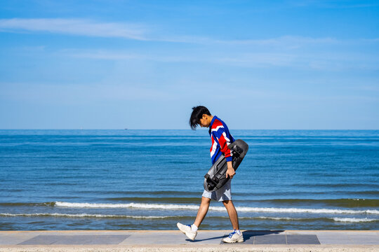 Man teennager wearing sportwear and shoes playing,walking and holding surf skate on the road oudoor in the morning. Relax and enjoy extreme surfskate on summer holiday at the beach.