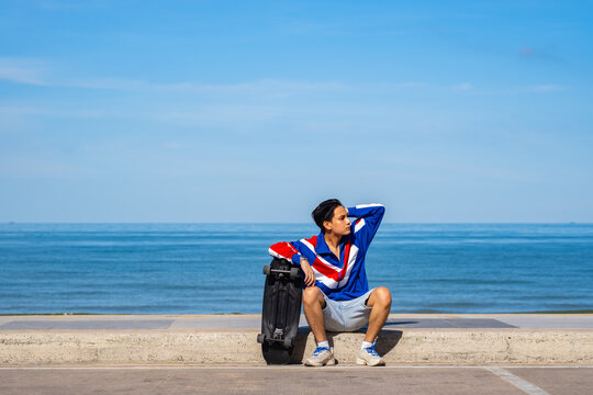 Man teennager wearing sportwear and shoes playing,sitting and holding surf skate on the road oudoor in the morning. Relax and enjoy extreme surfskate on summer holiday at the beach.