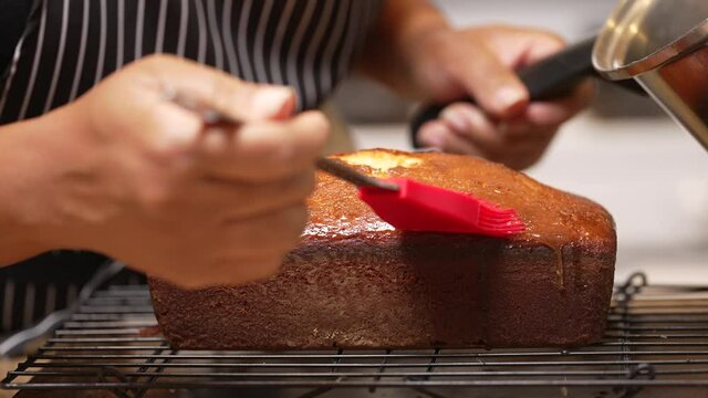 Drizzling and brushing a sugar glaze on a freshly baked lemon pound cake - slow motion