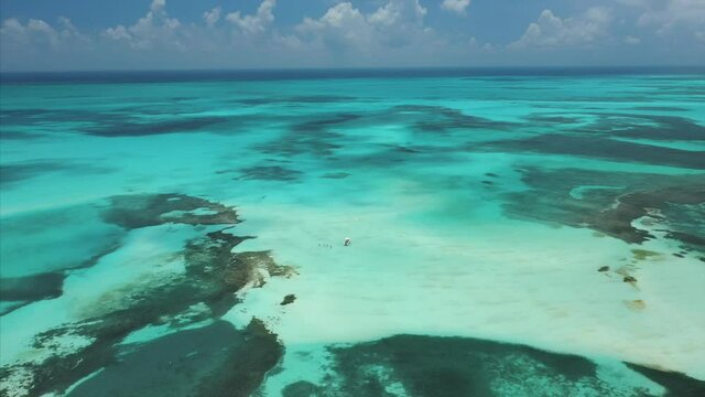 Aerial Drone view of a boat with people on a white and blue sandbar in the Caribbean. Turquoise water with moving clouds.