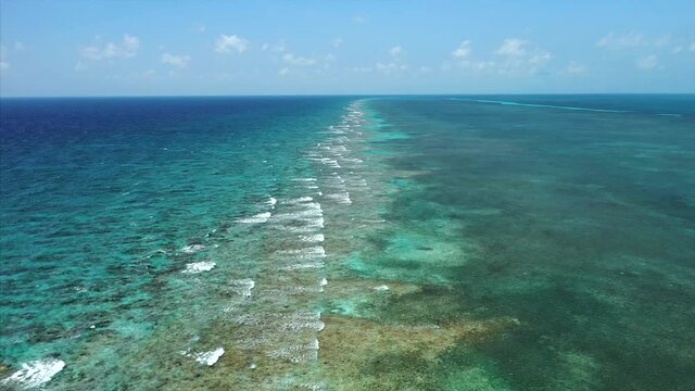 Aerial Drone flying over the Caribbean Barrier Reef in Belize. Waves crashing on coral. Shades of Blue.