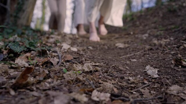 three women passing the camera on a path. They are wearing white robes and they are barefooted.