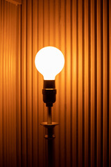 Gros plan sur une ampoule allumée sur une lampe en avant d'un mur en bois