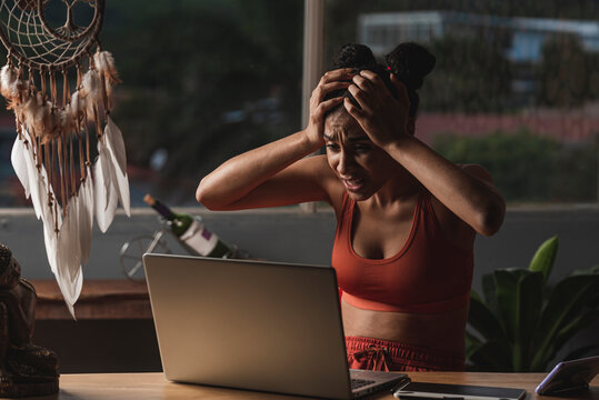 mujer morena sorprendida con las manos en su cabeza y muy asustada con su computadora haciendo tele trabajo 