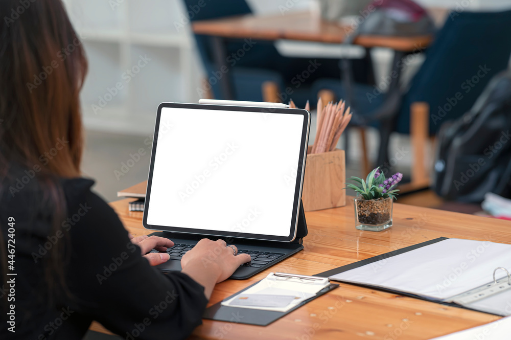 Wall mural Rear view of businesswoman working on tablet with blank screen while sitting at the table in office.