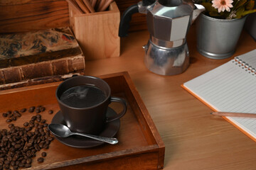 Cup of coffee with roasted coffee beans and moka pot on wooden table.