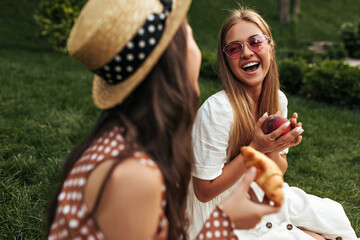 Good-humored blonde tanned lady in stylish red sunglasses and white dress laughs, talks to her...