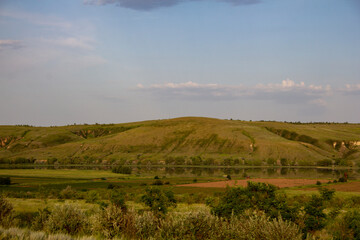 The calm wide river carries its waters under the morning sky. Landscape with hills, trees and a river in Russia