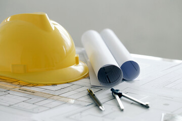 Yellow hard safety helmet hat and the blueprint, pen, ruler, protractor, and tape measure on the...