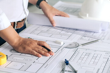 Close up of engineer working on blueprint architectural project at construction site at desk in...