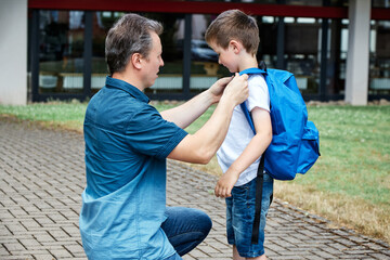 Dad, dad puts a blue backpack on his son. Parents accompany their children to school, first grade....