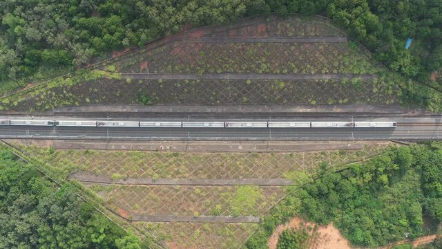 Aerial top view of a long white high-speed train driving through the slope protection railway line in China