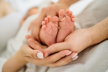 Closeup of parents hands holding newborn baby feet with wedding rings. Relation, love, childbirth and new family.