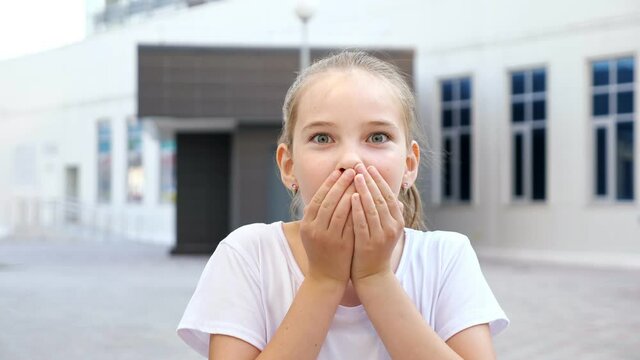 Girl shows amusement looking straight. Blonde teenager with ponytail performs shock and happiness posing for camera standing on city street closeup