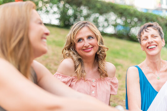 Close up view of three adult women sitting in the park laughing