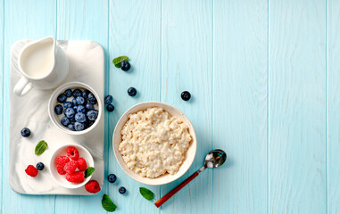 Obraz na płótnie Canvas Bowls of oatmeal porridge with blueberries and raspberries on a marble board. Top view flat lay. Healthy breakfast and diet food. Porridge with fresh berries and almond slices on blue table.