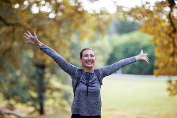 A young woman with happy face expression and spread arms dressed in outdoor sports clothes is...