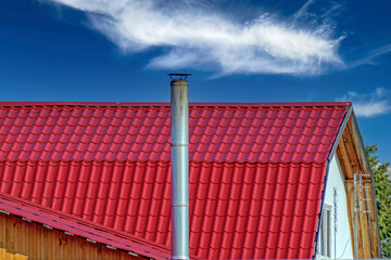 A fragment of the roof of a village house against the background of a blue sky with white clouds
