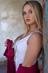 Portrait of young beautiful blond modern female dancer in white corset, red dress and red long socks inside old house between rustic walls in ambient lighting