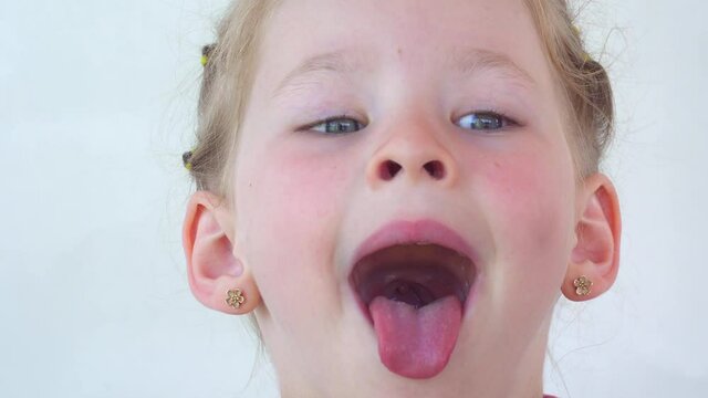 little girl show tongue, throat. portrait with wide open mouth and protruding tongue. with clear view pulls out long tongue. soft palate and mouth to dentist. mouth is wide open, tongue is stuck out.