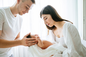 Young parents gently look at their newborn baby. A man, father carefully holding a sleepless baby girl in their arms. A woman mother lovingly embraces her daughter.
