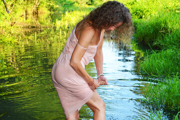 A young girl comes out of the river wringing out a wet dress