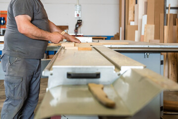 man's hands cutting some wooden boards on an industrial machine in a carpentry workshop and with many wooden boards in the background