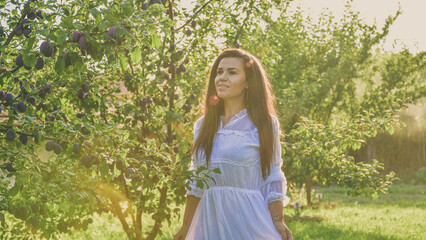 Fototapeta na wymiar Young beautiful smiling woman with romantic dress at orchar near a plum tree. Young pretty farmer woman