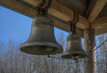Obraz premium Cast bells on a wooden rural bell tower on a sunny spring day. A pair of large heavy bells against the blue sky. The inscription on one of the bells 