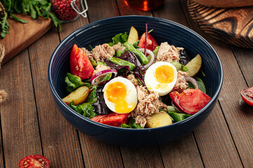 Tuna salad with eggs and vegetables on a wooden background