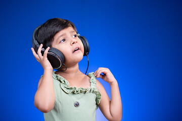 Happy liitle kid with headphones enjoying favourite song by singing loudly on blue background.