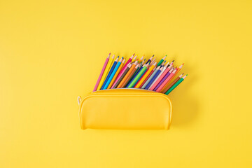 Yellow pencil case with colored pencils on yellow background. Back to school. Flat lay, top view,...