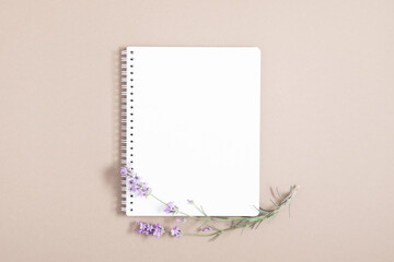 White notebook cover and sprig of lavender on beige background. Flat lay, top view, copy space
