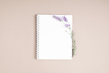 White notebook cover and sprig of lavender on beige background. Flat lay, top view, copy space