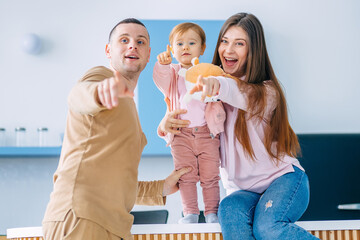 Family happiness. Cheerful parents spend time with their adorable daughter in the kitchen, saw something and point with their fingers